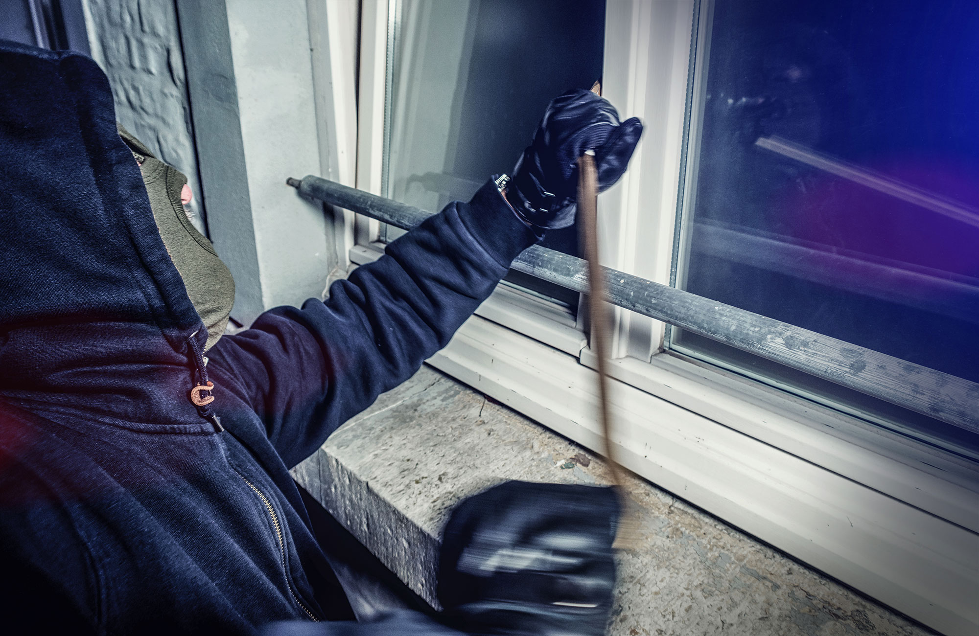 Burglar with crowbar breaking window